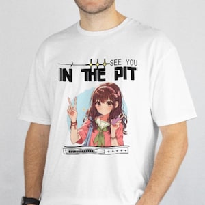 May include: White t-shirt featuring an anime-style illustration of a girl making a peace sign. The text "SEE YOU IN THE PIT" is printed above the illustration in black. The girl is wearing a pink jacket and holding a phone.