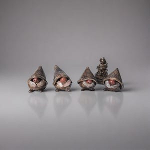 May include: A collection of small, handcrafted gnome figurines. Each gnome has a pointed hat with a textured pattern, a white beard, and a smiling face. The gnomes are brown and tan, with a small, abstract sculpture in the background.