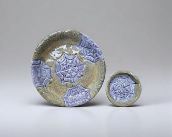 May include: A ceramic plate and small bowl set. The plate and bowl are beige with a blue-purple spiderweb design. The plate is round and the bowl is small and round. The set is handmade.
