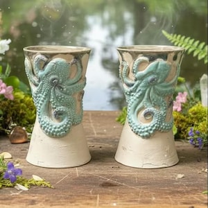 Puede incluir: Dos vasos de cerámica con un diseño de pulpo en relieve y texturizado en color verde azulado claro. Las tazas tienen una base lisa de color blanco roto con un borde acampanado y un cuerpo cónico, mostrando ventosas y tentáculos detallados.