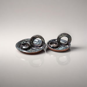 Puede incluir: Dos platos de cerámica para anillos con un esmalte azul oscuro y verde. Cada plato tiene un cuenco pequeño y redondo y un asa de anillo más grande. Los platos están sobre una superficie reflectante.