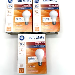 May include: Three boxes of GE soft white light bulbs. Each box displays a 40W bulb, using only 29W, with a 1.1-year life. The boxes have orange and white accents, and the text "Longer Life" and "Uses 28% Less Energy" are visible.