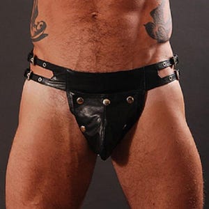 Puede incluir: Jockstrap de cuero negro con remaches y hebillas plateadas. El jockstrap presenta una bolsa contorneada y una cintura ancha con dos correas ajustables. La prenda está diseñada para un ajuste ceñido.