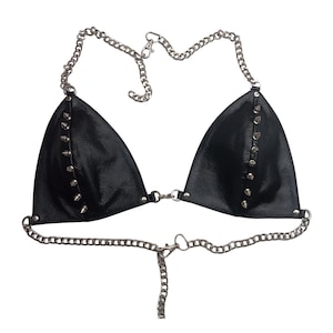 May include: Black leather bikini top with silver-colored chain straps and accents. The triangle cups are adorned with silver-colored spikes. The top is designed with a chain that goes around the neck and a chain that goes around the torso.