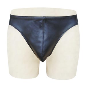 Puede incluir: Ropa interior negra hecha de un material liso, similar al cuero. La prenda se muestra en un maniquí, mostrando su diseño. La ropa interior tiene una cintura baja y un corte de calzoncillo.