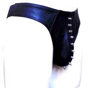 Puede incluir: Prenda de cuero negro con púas plateadas en el lateral. La prenda parece ser un tipo de ropa interior o parte inferior. El artículo se exhibe en un maniquí blanco.