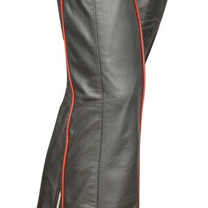May include: Black leather chaps with red trim. The chaps have a wide waistband with a buckle closure and a red accent on the front. A zipper runs along the outer seam of the leg.
