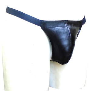 Puede incluir: Jockstrap de cuero negro con cinturilla elástica azul oscuro. El jockstrap está hecho de cuero liso y brillante y presenta una bolsa contorneada. La banda elástica está unida a la bolsa de cuero.