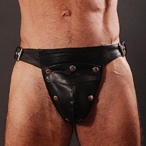 May include: Black leather jockstrap with a pouch and studded accents. The jockstrap features a belt-style closure with silver-tone buckles. The garment is designed with a contoured pouch and is made of a smooth, shiny leather material.