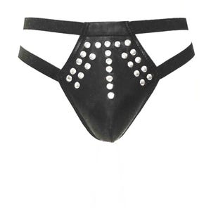 Puede incluir: Ropa interior de cuero negro con tachuelas plateadas. La ropa interior presenta un diseño geométrico con un patrón central tachonado y correas en los lados y la cintura. La prenda está diseñada para un ajuste ceñido.