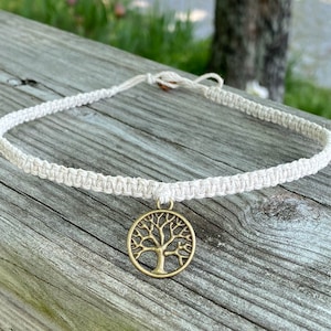 May include: A white macrame cord necklace with a gold tree of life pendant.