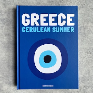 Könnte beinhalten: Ein blauer Buchumschlag mit dem Titel "GREECE CERULEAN SUMMER" und einem weißen und blauen bösen Auge. Das Buch wird von REMINISCENCE herausgegeben.