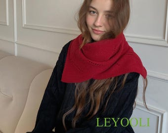 May include: A red knit scarf with a decorative edge is worn over a black cable-knit sweater. The scarf is draped around the neck. The word "LEYOOLI" is printed in green on the lower right side of the image. The person is sitting on a white couch.