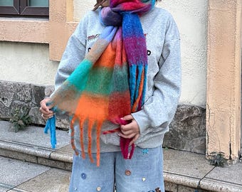 Könnte beinhalten: Ein mehrfarbiger Schal mit Fransen in Rot-, Orange-, Grün- und Blautönen. Der Schal ist um den Hals gewickelt. Er hat eine weiche, flauschige Textur und ist ein auffälliges Accessoire.