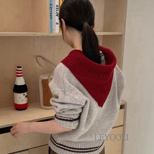 May include: A light gray knit sweater featuring a deep red triangular hood with a textured pattern, long sleeves with dark brown striped cuffs, and a matching striped hem. The word LEYOOLI is printed in blue on the lower right side of the sweater.