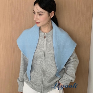 May include: A light gray zip-up sweater with a light blue shawl collar. The sweater has ribbed cuffs and hem. The model is wearing white pants. The background is a light brown wooden wall.