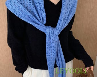 Könnte beinhalten: Ein hellblauer, offen gewebter Schal ist über einem schwarzen Pullover drapiert und vorne geknotet. Der Schal hat ein zartes, rautenförmiges Muster. Das Outfit wird durch eine weiße Hose und eine braune Handtasche ergänzt.