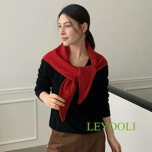 Puede incluir: Una mujer con un suéter negro y una bufanda roja sobre los hombros. También lleva pantalones marrones y un bolso marrón. El texto "LEYOOLI" es visible en la imagen.