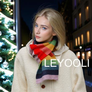 Może przedstawiać: Kobieta w białym płaszczu z kolorowym, paskowanym szalikiem. Szalik ma czerwone, żółte, zielone, niebieskie i różowe paski. Na szaliku widoczny jest napis "LEYOOLI".