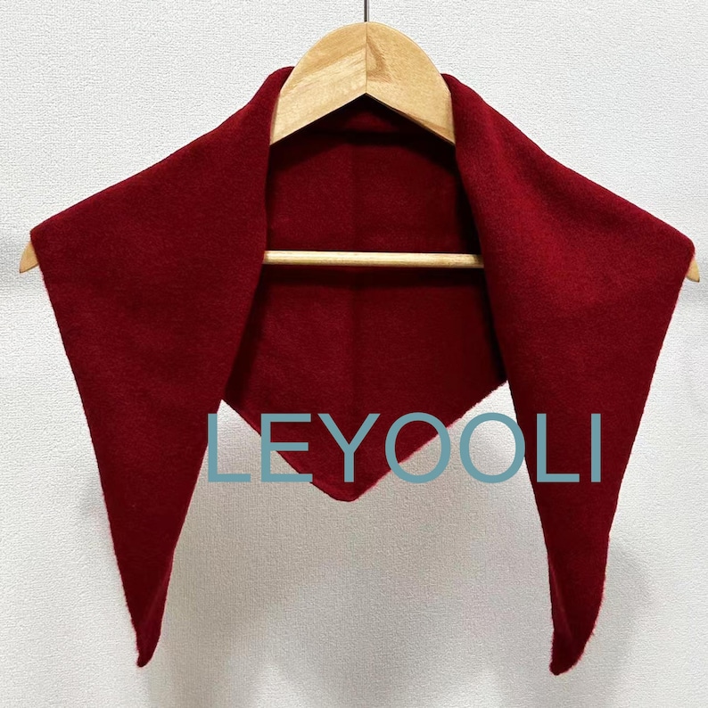 May include: A red triangular scarf hanging on a wooden hanger. The scarf is made of a soft, fuzzy material. The word "LEYOOLI" is printed in white on the scarf.