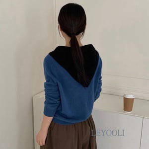 Puede incluir: Un suéter de punto de manga larga con cuerpo azul y una sección de cuello en V negra en contraste. La prenda tiene dobladillo y puños acanalados, y el texto LEYOOLI está impreso en azul en la parte inferior derecha de la tela.
