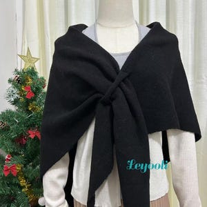 Könnte beinhalten: Ein schwarzer Schal aus weichem, strukturiertem Stoff ist über einer Schaufensterpuppe drapiert und vorne gebunden. Der Hintergrund umfasst einen Weihnachtsbaum mit goldenen Sternen und roten Schleifendekorationen. Das Wort "Leyooli" ist unten rechts sichtbar.