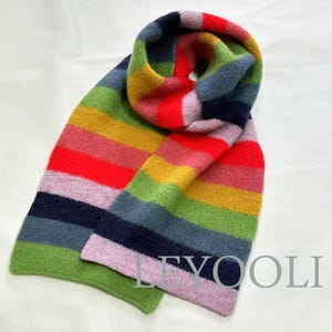 May include: A colorful striped scarf with a rainbow pattern in shades of red, pink, yellow, green, blue, and purple. The scarf is made of a soft, fuzzy material and is perfect for adding a pop of color to any outfit.