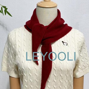 May include: A red knitted scarf tied around a white cable knit sweater with the word "LEYOOLI" printed on the front.