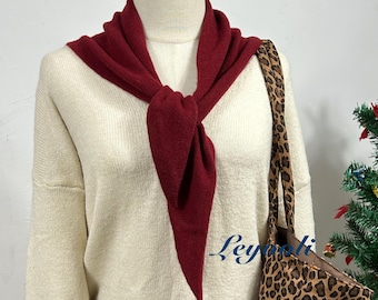 May include: A burgundy-colored scarf is draped over a cream-colored sweater. The scarf is knotted at the front, creating a stylish accent. A leopard print tote bag is visible on the right side of the image. The scarf adds a pop of color to the neutral-toned outfit.