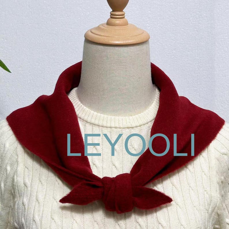 May include: A red knit scarf tied in a bow around a white sweater. The scarf is made of a soft, fuzzy material. The text "LEYOOLI" is printed on the scarf.