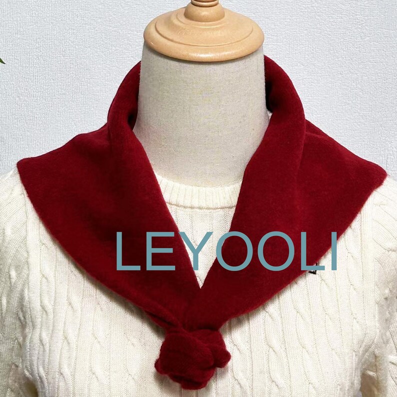 May include: A red fleece neck warmer with a knotted bow at the front. The neck warmer is worn on a white sweater.