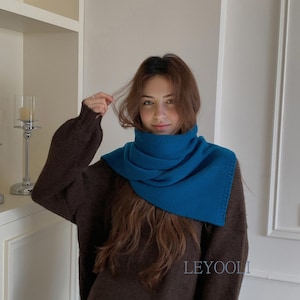 Könnte beinhalten: Ein dunkelbrauner Langarmpullover kombiniert mit einem leuchtend blaugrünen Strick-Halswärmer. Der Pullover hat einen gerippten Kragen, Bündchen und Saum, während der Halswärmer ein strukturiertes Strickmuster aufweist. Der Text LEYOOLI ist auf dem Pullover zu sehen.