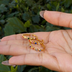 May include: Three gold rings with colorful gemstones. The rings are stacked on top of each other and feature a variety of colors, including red, blue, green, and purple.