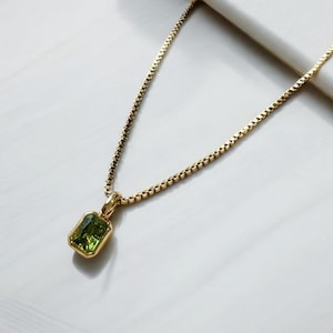 Peut inclure: Un collier en chaîne dorée avec un pendentif en pierre précieuse verte. Le pendentif est de forme rectangulaire avec une surface lisse et polie.