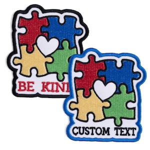 May include: Two embroidered patches featuring puzzle pieces in red, blue, yellow, and green, with a white heart. One patch reads "BE KIND" in red text, and the other says "CUSTOM TEXT" in blue text. Both have a black border.
