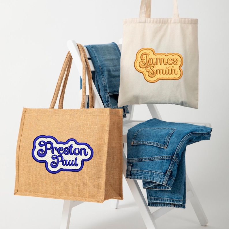 May include: Two tote bags with personalized embroidered names. The bag on the left is a brown jute tote bag with the name "Preston Paul" embroidered in blue. The bag on the right is a white canvas tote bag with the name "James Smith" embroidered in yellow.