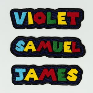 May include: Three embroidered patches with names: VIOLET, SAMUEL, and JAMES. Each name is in colorful, block letters with a denim-like border. The letters are in shades of blue, red, yellow, and green.