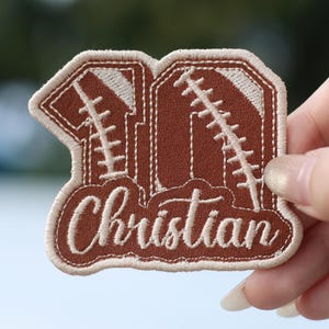 May include: A brown leather patch with a white stitched outline in the shape of the number 10. The number 10 is made to look like a football. The name Christian is stitched in white on the bottom of the patch.