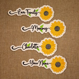 May include: Four white iron-on patches with sunflower designs and personalized text. The patches feature a yellow sunflower with a brown center and green leaves. The text on the patches reads "Love Family", "Mommy", "Charlotte", and "Your Name".