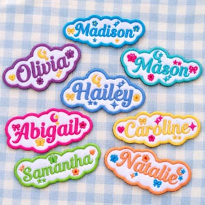 May include: A collection of eight cloud-shaped embroidered patches featuring names in various colors including blue, purple, teal, pink, yellow, green, and orange. Each patch is decorated with small icons like stars, moons, bows, and flowers.