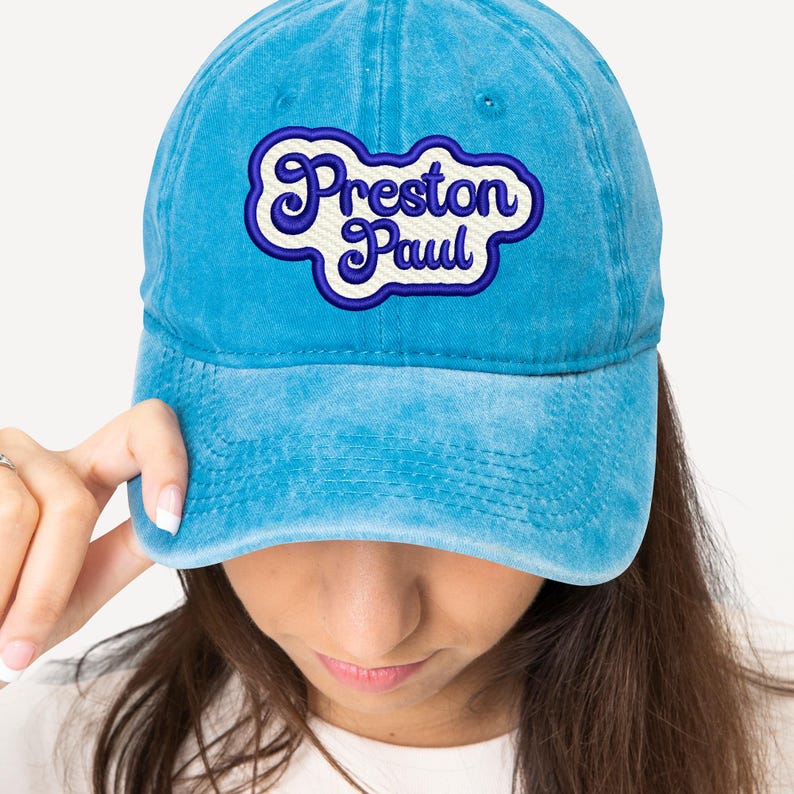 May include: A blue denim baseball cap with a white and blue embroidered patch that says "Preston Paul" in a retro font.