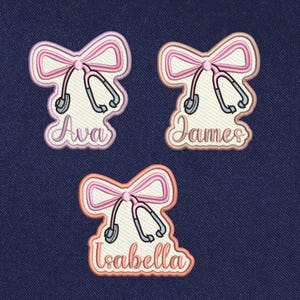 May include: Three embroidered iron-on patches with pink bows and a stethoscope. The patches are personalized with the names Ava, James, and Isabella.