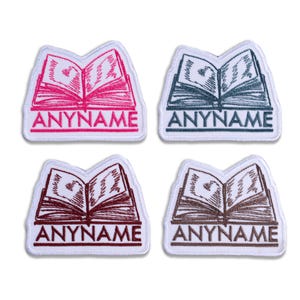 May include: Four embroidered patches featuring an open book design. Each patch has a different color: pink, blue-gray, burgundy, and brown. The text "ANYNAME" is below the book on each patch.