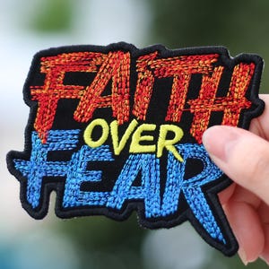 May include: Embroidered patch with the words "Faith Over Fear" in a bold, colorful font. The word "Faith" is in red and orange, "Over" is in yellow, and "Fear" is in blue.