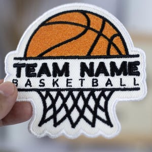 May include: White embroidered patch with a basketball, a basketball hoop, and the text "TEAM NAME BASKETBALL".