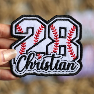 May include: White baseball-themed iron-on patch with the number 28 and the name Christian in black cursive lettering.
