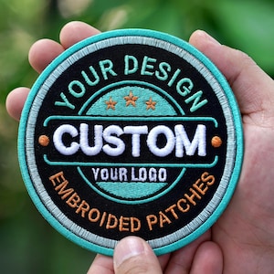 May include: Round embroidered patch with the text "YOUR DESIGN CUSTOM YOUR LOGO EMBROIDERED PATCHES". The patch has a black background with teal and white accents, and three orange stars.