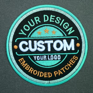 Pu&ograve; includere: Toppa rotonda ricamata con le scritte "YOUR DESIGN" e "EMBROIDERED PATCHES". La toppa ha uno sfondo nero con dettagli bianchi e turchese. La parola "CUSTOM" &egrave; in bianco e "YOUR LOGO" &egrave; sotto.