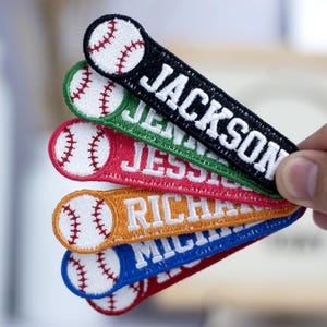 May include: Five personalized baseball-themed iron-on patches with different names: Jackson, Jenna, Jessie, Richard, and Michael. Each patch features a white baseball with red stitching and a white name in a different color: black, green, red, orange, and blue.
