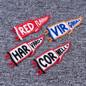 May include: Four embroidered patches in a pennant shape with the words "RED FLASH", "VIRGINIA", "HARVARD", and "CORNELL" in white lettering. Each patch has a red or black border and small red accents, set against a gray textured background.